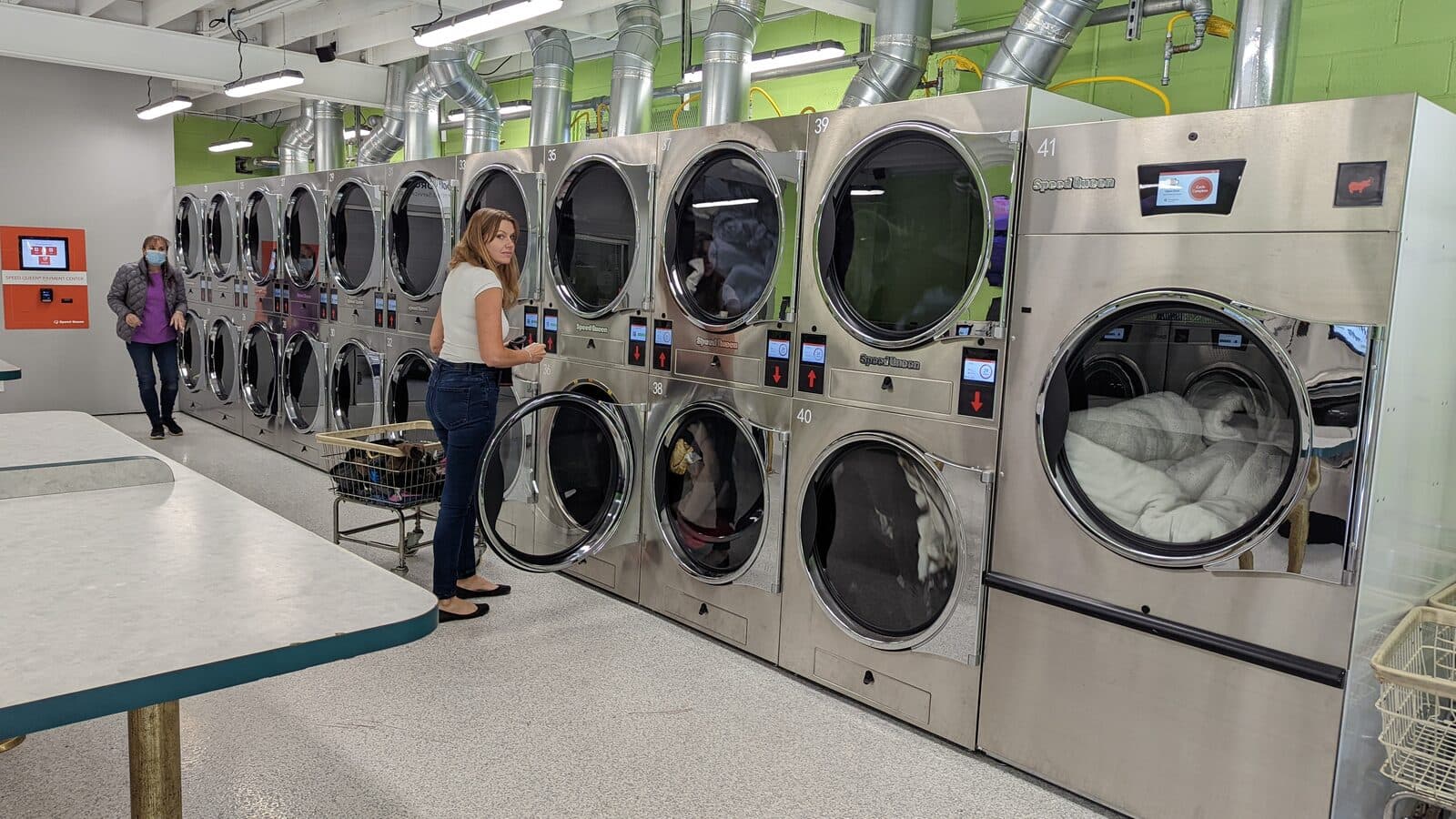 Rows of stainless Speed Queen washers and dryers inside The Mat, with daylight coming through the windows